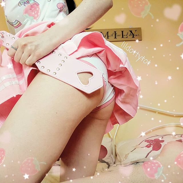 Aesthetic lifestyle shot of a model wearing a kawaii pink pleated skirt with the pink heart spanking paddle peeking into the frame.