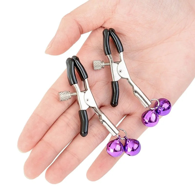 A lifestyle shot showing a person's open palm holding a pair of silver adjustable nipple clamps with black rubber tips and purple bells. This image clearly demonstrates the small, beginner-friendly size, lightweight design, and actual scale of the toy.