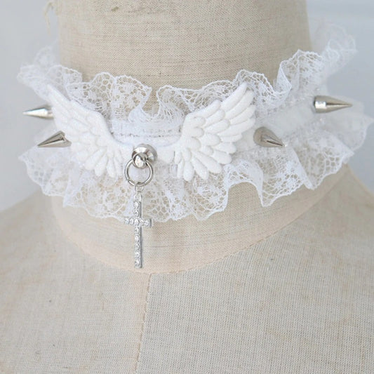 Product shot of a white pastel goth ruffled lace choker featuring white angel wings, silver metal spikes, a rhinestone cross pendant, and an adjustable silver clasp.