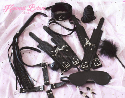 Aesthetic flat lay of the complete black bondage kit resting on ruffled white bed sheets.