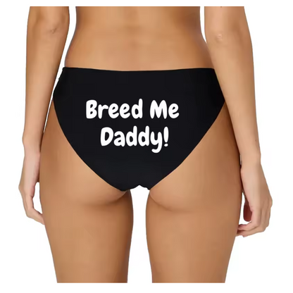 Model posing in black bikini panties with white 'Breed Me Daddy!' slogan. Kinky breeding fantasy lingerie.