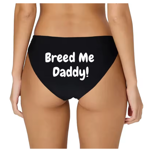 Model posing in black bikini panties with white 'Breed Me Daddy!' slogan. Kinky breeding fantasy lingerie.