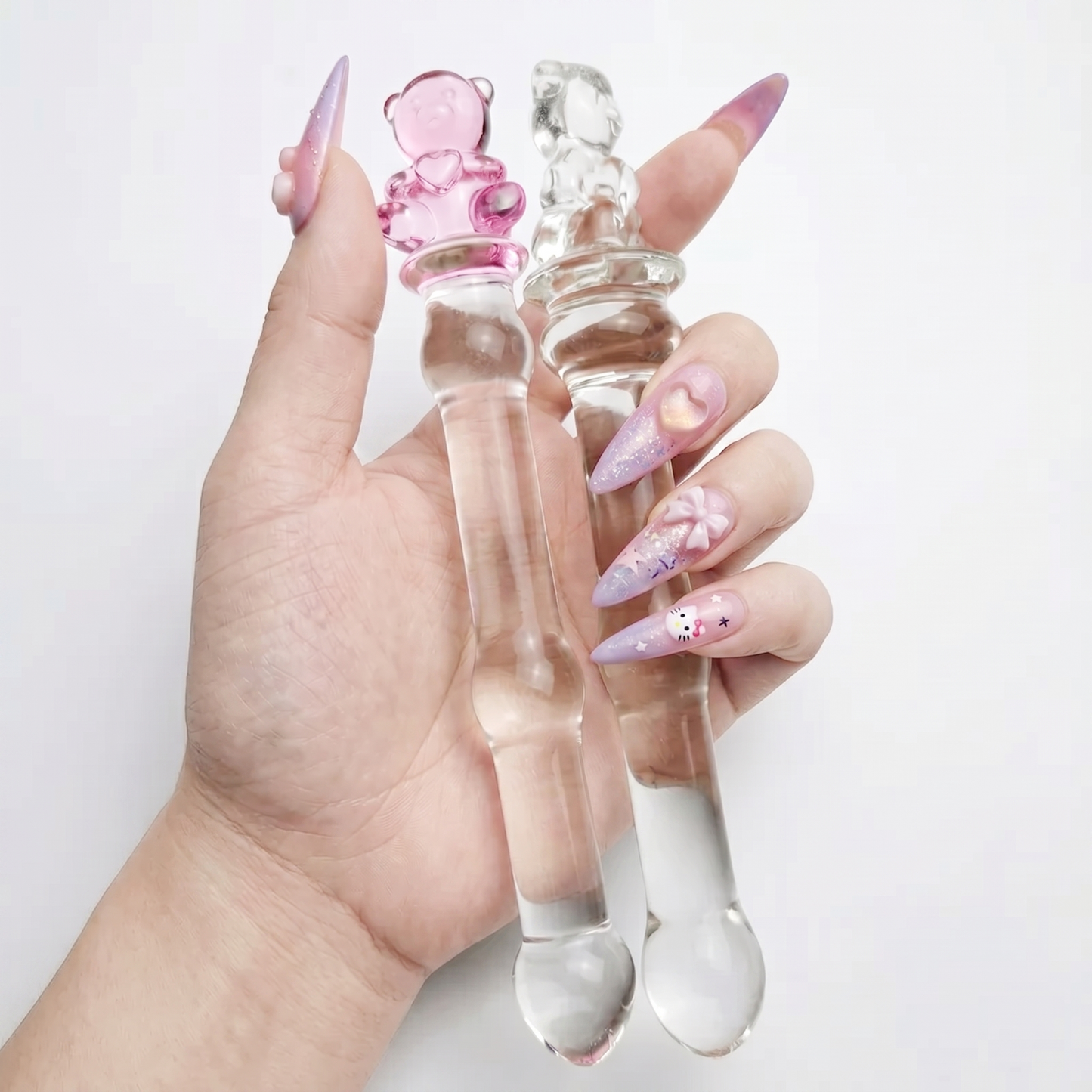 Hand with long aesthetic nails gripping the slim clear glass shaft of the pink teddy bear wand.