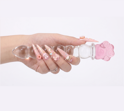 Hand holding the glass wand horizontally against a white background to display the ribbed design and pink paw handle.