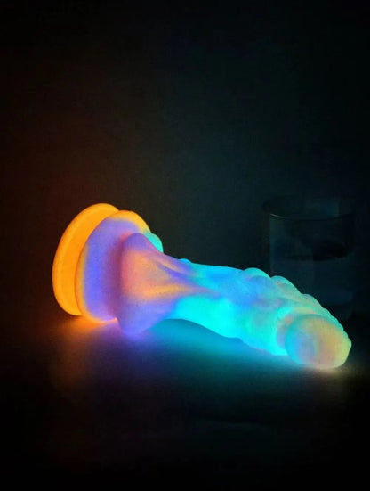 The luminous dragon dildo glowing magically in the dark with bright neon blue and orange hues while standing on its suction cup.