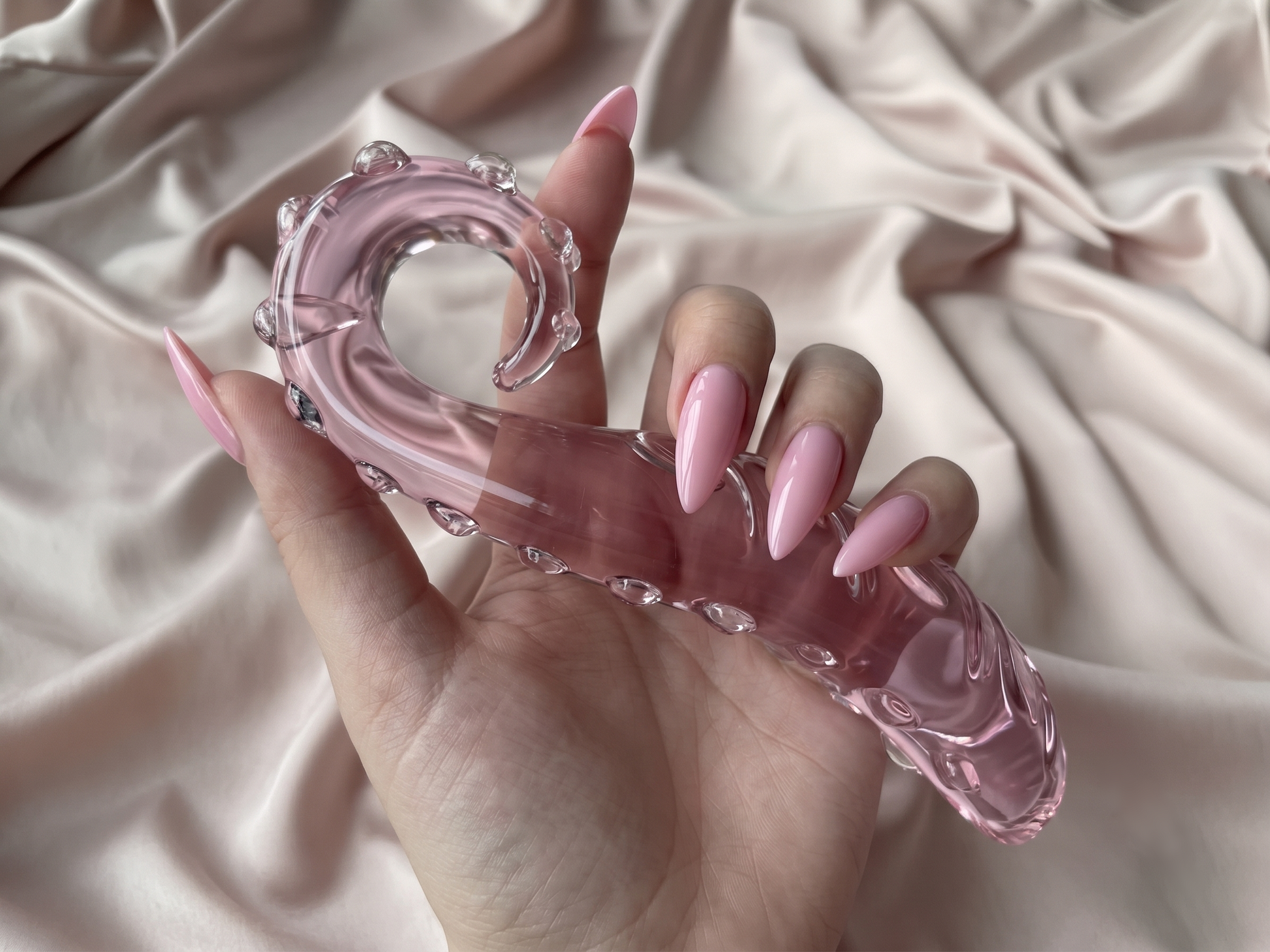 Hand showing the ergonomic grip of the crystal clear thick curl glass fantasy wand against a champagne silk background.