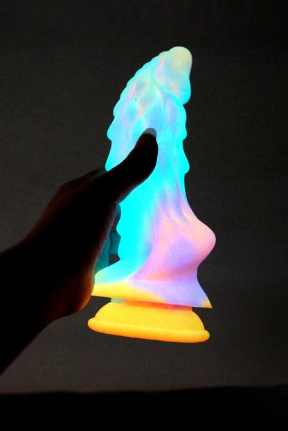 Silhouette of a hand holding the fantasy dragon dildo as it powerfully glows in the dark against a black background.