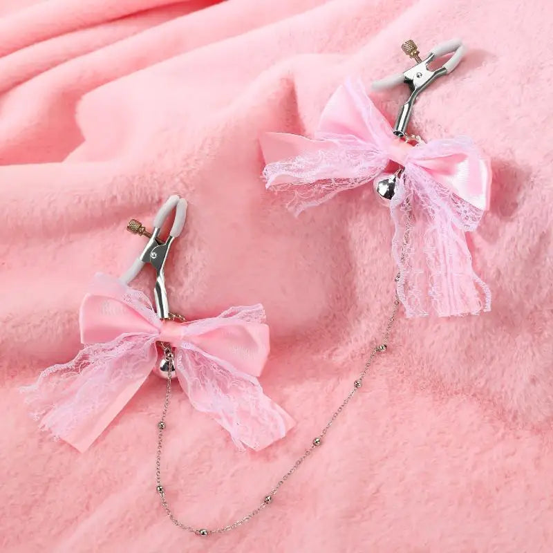 Close-up of the sweet pink ribbon nipple clamps with rubber tips and silver bells resting on a soft, pastel pink plush blanket.