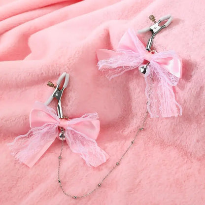 Close-up of the sweet pink ribbon nipple clamps with rubber tips and silver bells resting on a soft, pastel pink plush blanket.