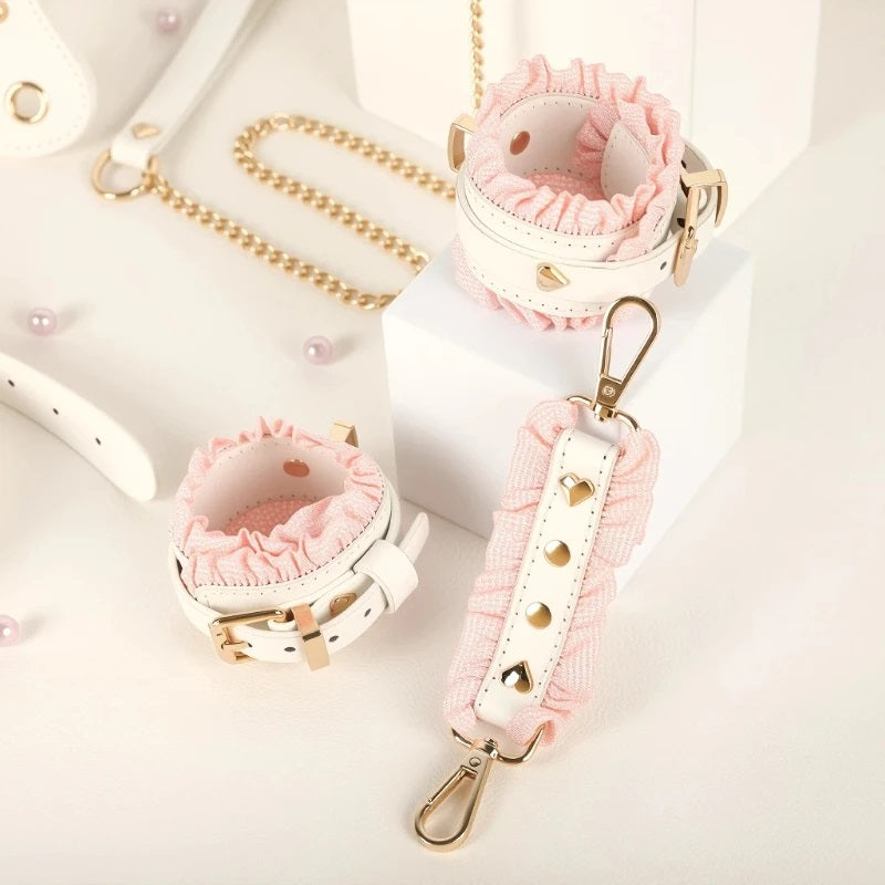 Close-up of the white leather cuffs with pink ruffles connected by a high-end rose gold clasp and studded link ribbon, resting on a white display stand.