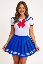 Model wearing a short-sleeved white onesie with blue sailor collar, red chest bow, and matching blue pleated schoolgirl skirt with white stripes, standing