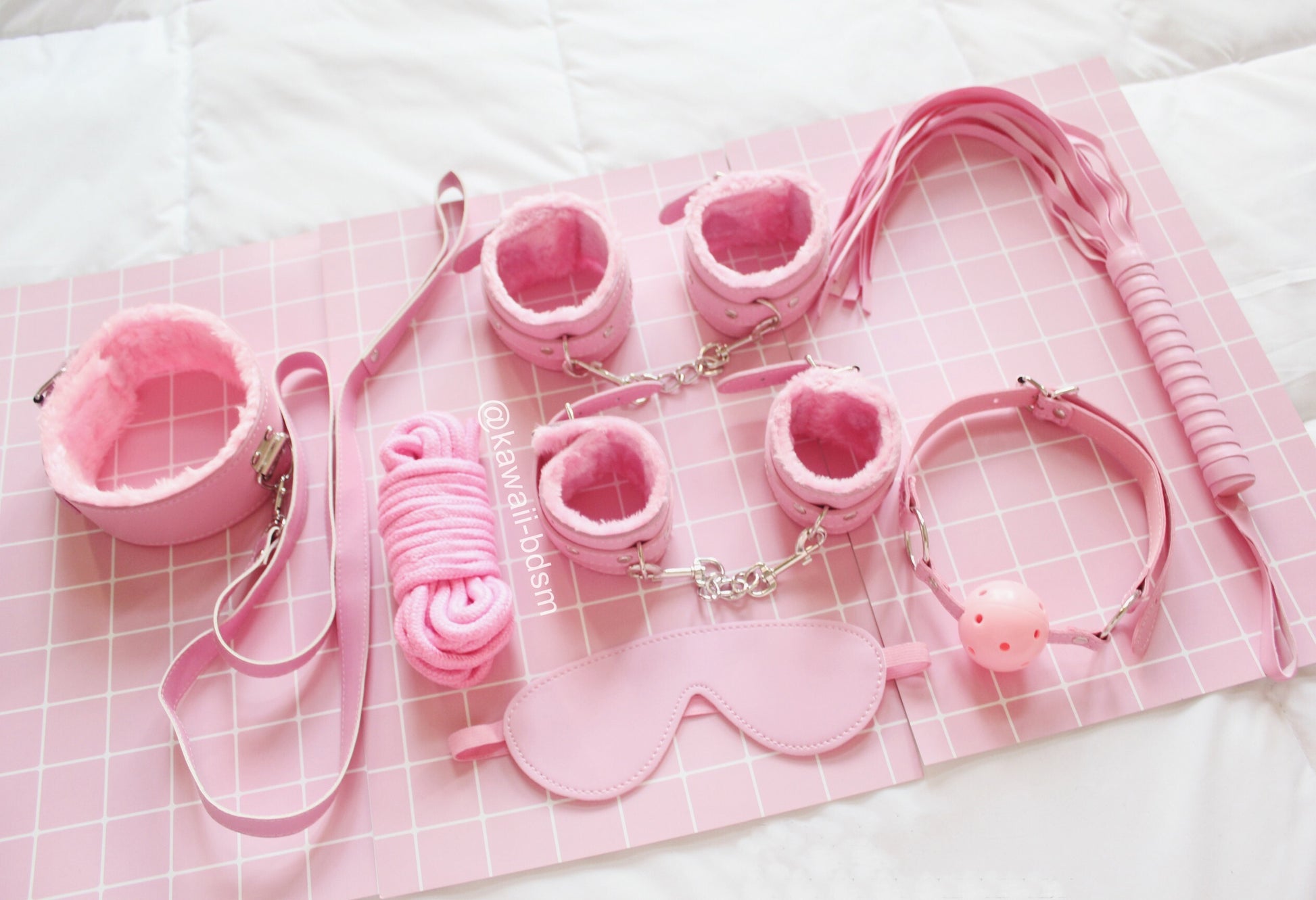 Pastel pink 7-piece bondage set arranged aesthetically on a soft pink blanket.