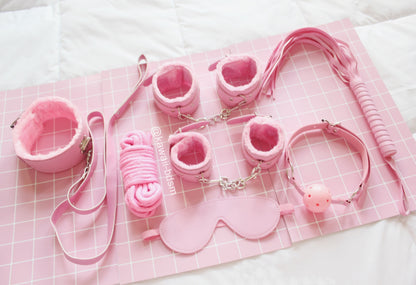 Pastel pink 7-piece bondage set arranged aesthetically on a soft pink blanket.