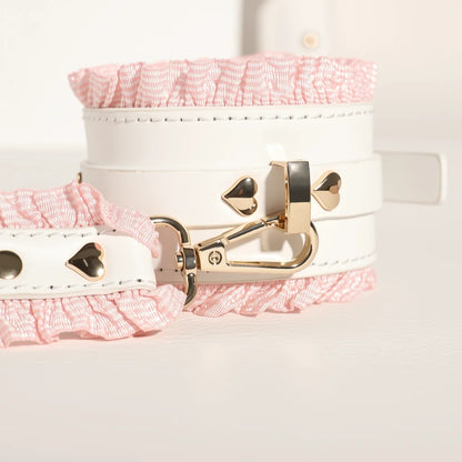 Close-up shot of the white vegan leather collar featuring a cute heart-shaped gold buckle, a pink ruffled lining, and a detachable rose gold chain leash.