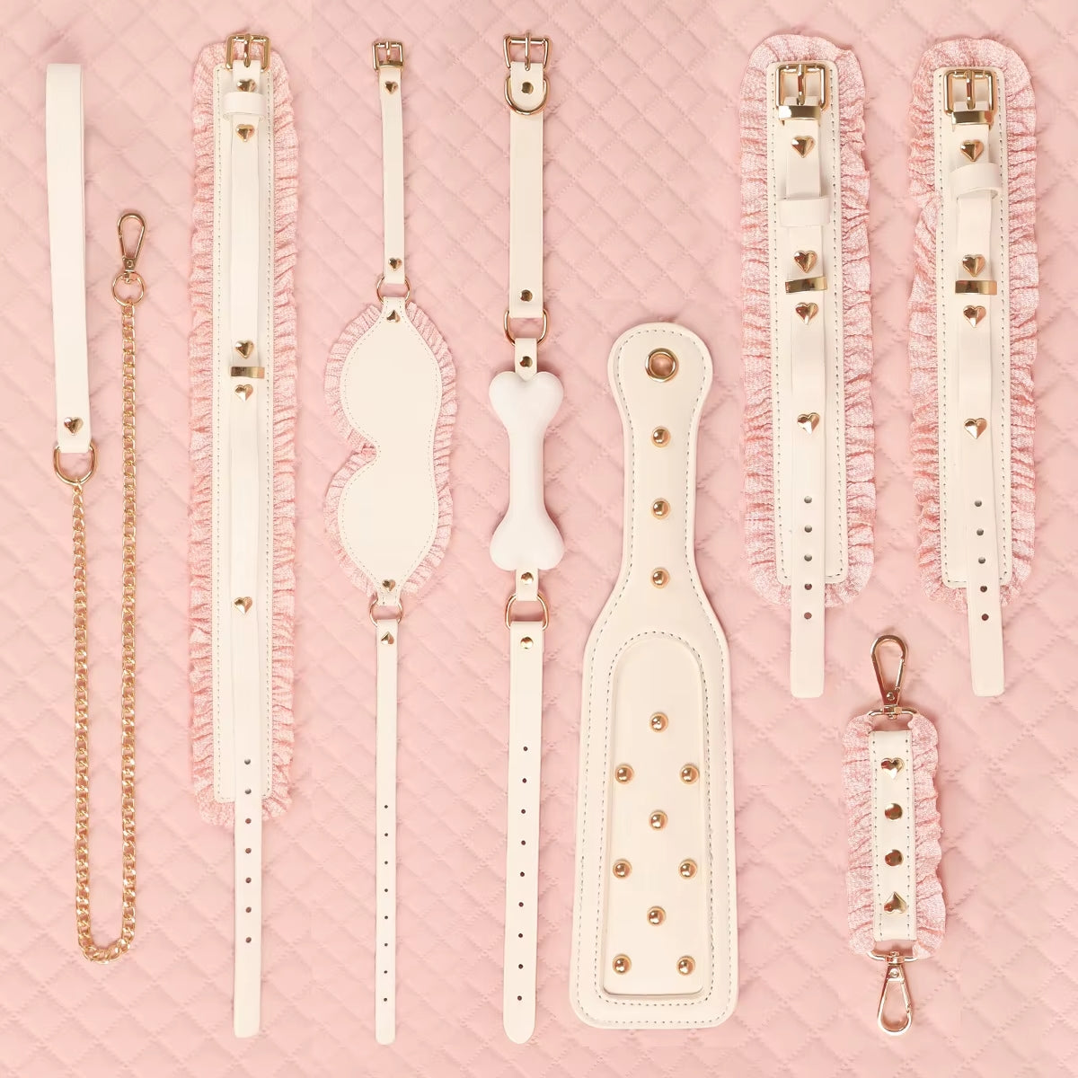 A clean grid lineup of all pieces in the white and pink bondage collection, displaying the paddle, straps, blindfold, and collars laid out perfectly on a blush pink background.