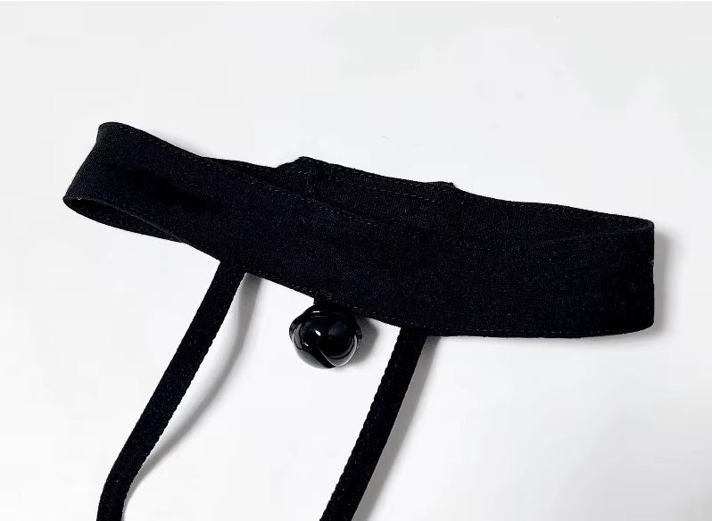 Close-up of a black velvet kitten play collar with a silver bell, connected to a strappy chest harness with satin bat wings.