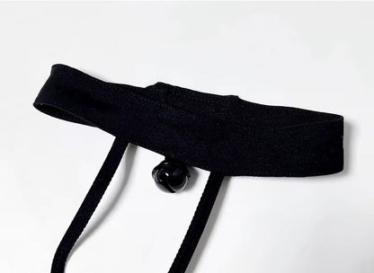 Close-up of a black velvet kitten play collar with a silver bell, connected to a strappy chest harness with satin bat wings.