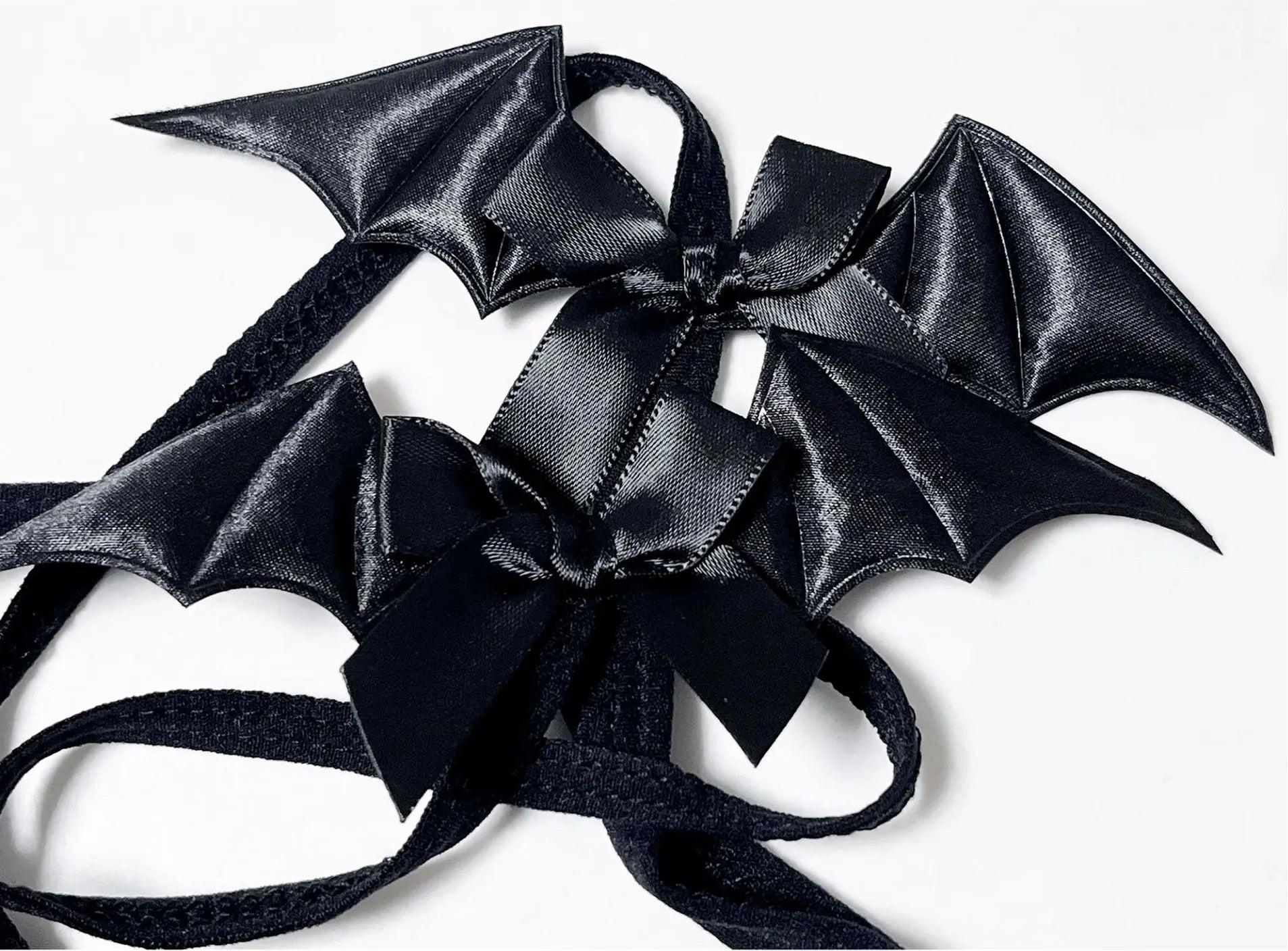 Close-up detail of the glossy black satin bat wing and ribbon bow on a kawaii goth elastic body harness.