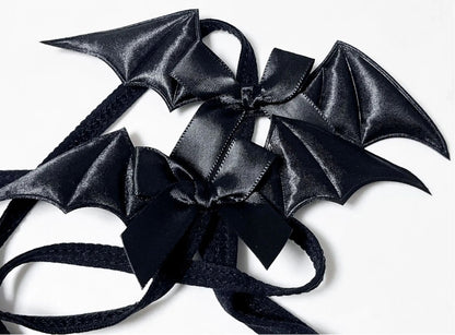 Close-up detail of the glossy black satin bat wing and ribbon bow on a kawaii goth elastic body harness.