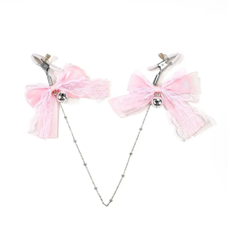 Adjustable nipple clamps featuring pink lace bows, silver jingle bells, and a connecting silver chain, laid out on a white background.