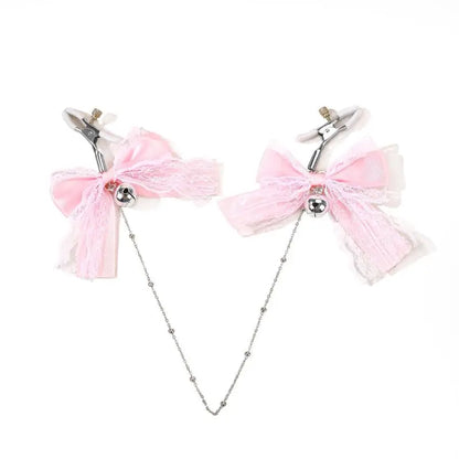 Adjustable nipple clamps featuring pink lace bows, silver jingle bells, and a connecting silver chain, laid out on a white background.