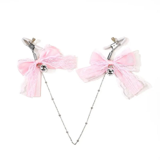 Adjustable nipple clamps featuring pink lace bows, silver jingle bells, and a connecting silver chain, laid out on a white background.