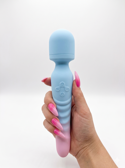A hand with long pink stiletto nails holds the blue and pink Sweet Surrender vibrator completely vertically against a white background.