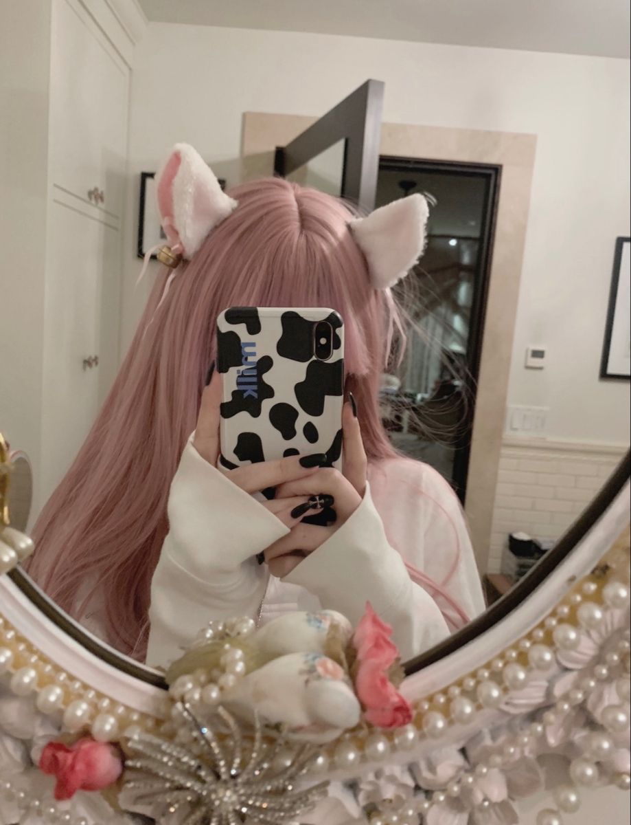 A girl with pink hair taking a mirror selfie while wearing kawaii kitten play ear clips.