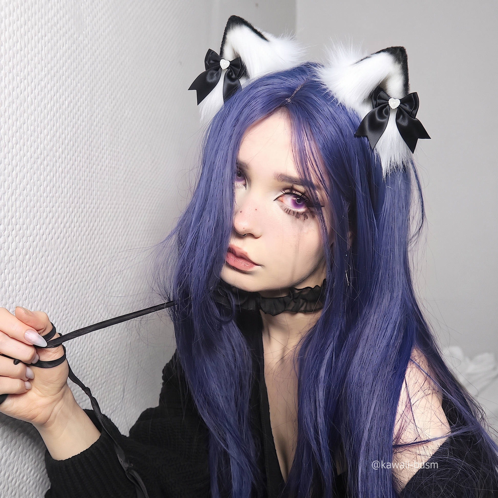 A lifestyle shot of an alternative model with long purple hair wearing a black collar and leash, elegantly styling the black and white fluffy pet play ear clips for a submissive aesthetic.