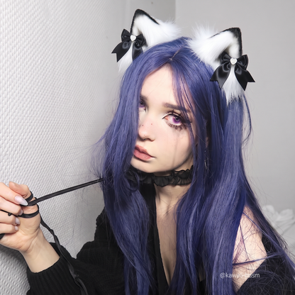 A lifestyle shot of an alternative model with long purple hair wearing a black collar and leash, elegantly styling the black and white fluffy pet play ear clips for a submissive aesthetic.