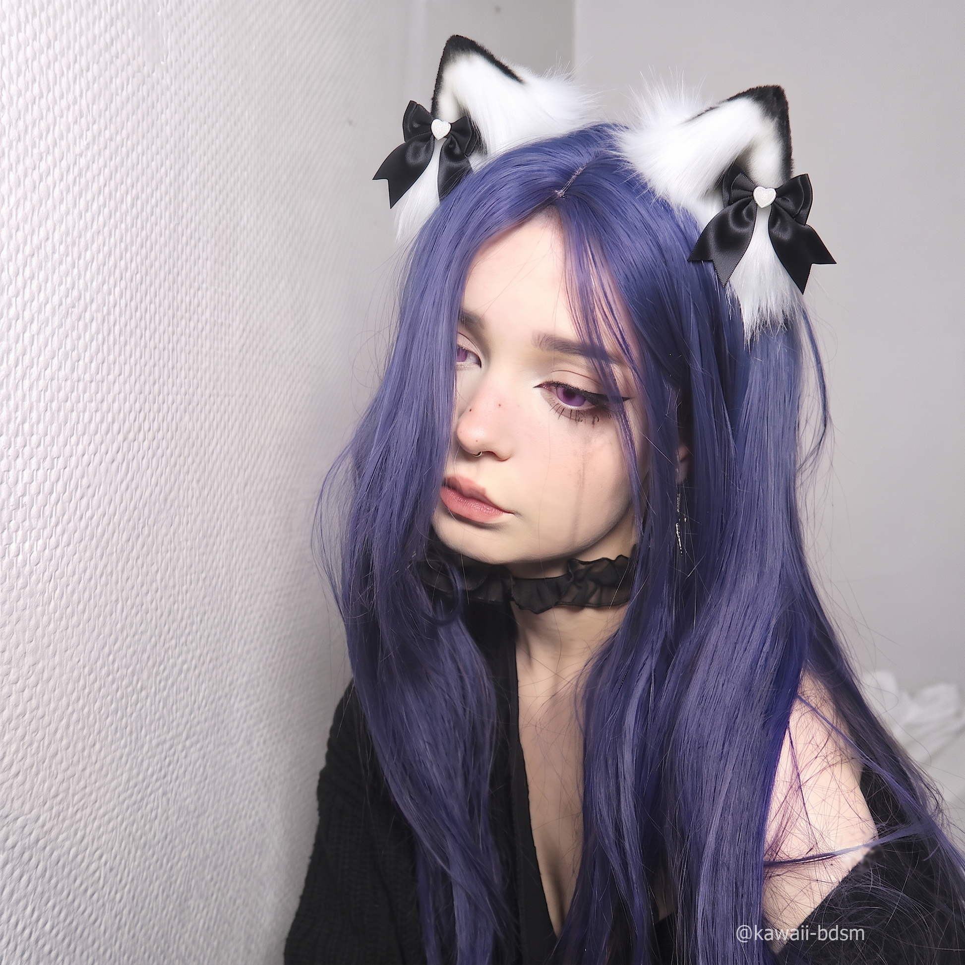 A close-up portrait of a model with purple hair looking softly into the camera, wearing the premium black and white fluffy cat ear clips with satin bows.