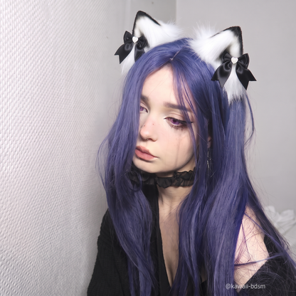 A close-up portrait of a model with purple hair looking softly into the camera, wearing the premium black and white fluffy cat ear clips with satin bows.
