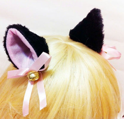 Black fluffy cat ear clips with pink satin bows worn in blonde hair.