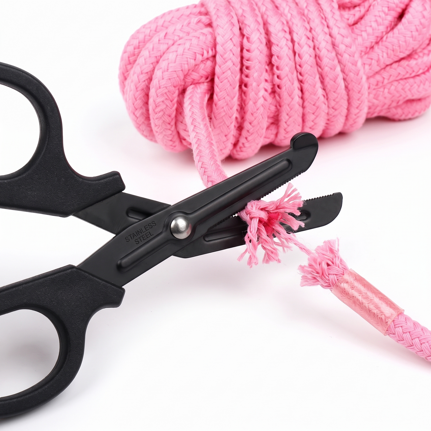 Macro close-up of the black serrated safety shears smoothly slicing through thick pink Shibari rope with precision and ease.