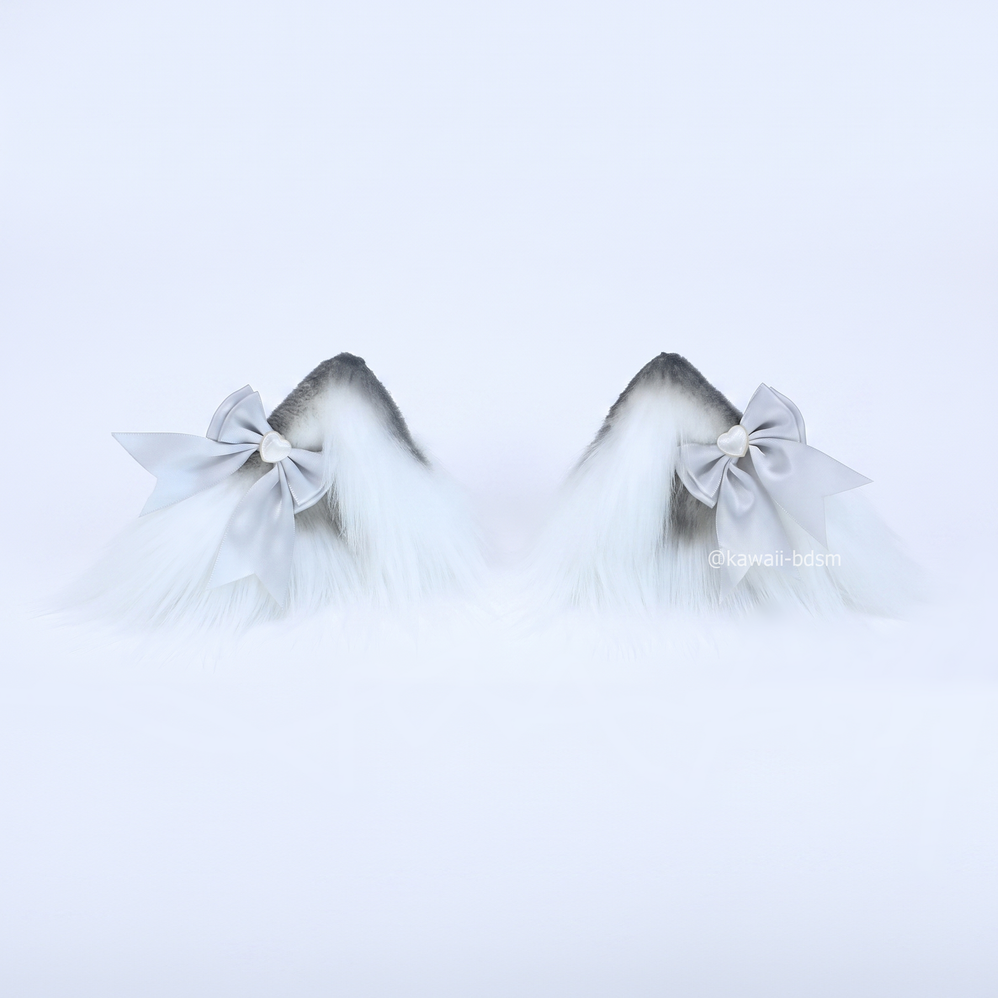 A pair of realistic fluffy wolf or kitten play ear clips featuring a white base with dark grey tips, styled with a silver satin bow and a small silver heart charm.