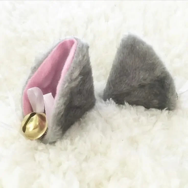 Grey furry ear clips with golden bells on a fluffy white background.
