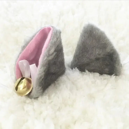 Grey furry ear clips with golden bells on a fluffy white background.