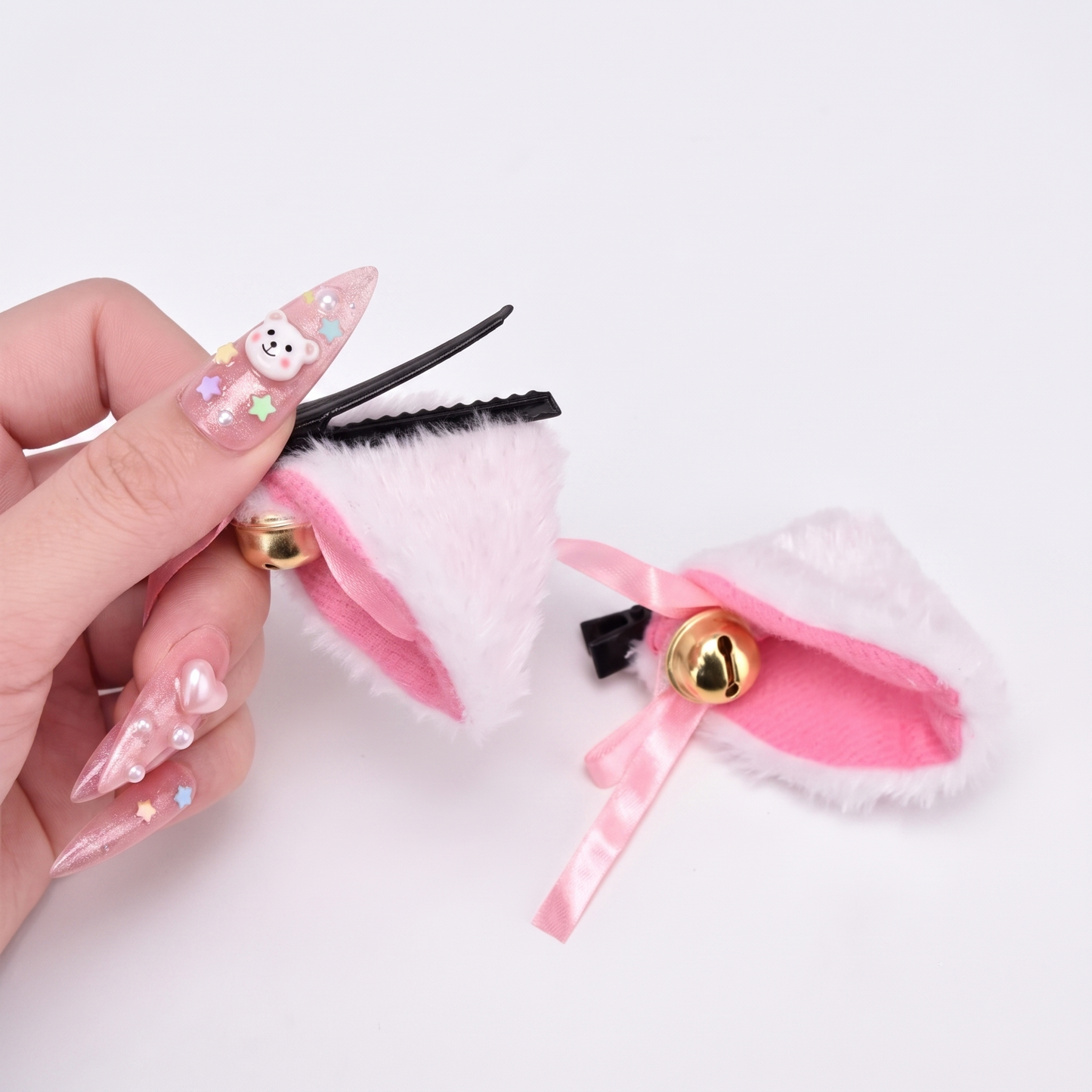 A hand with long pink nails elegantly holding a pink and white kitten play ear clip.