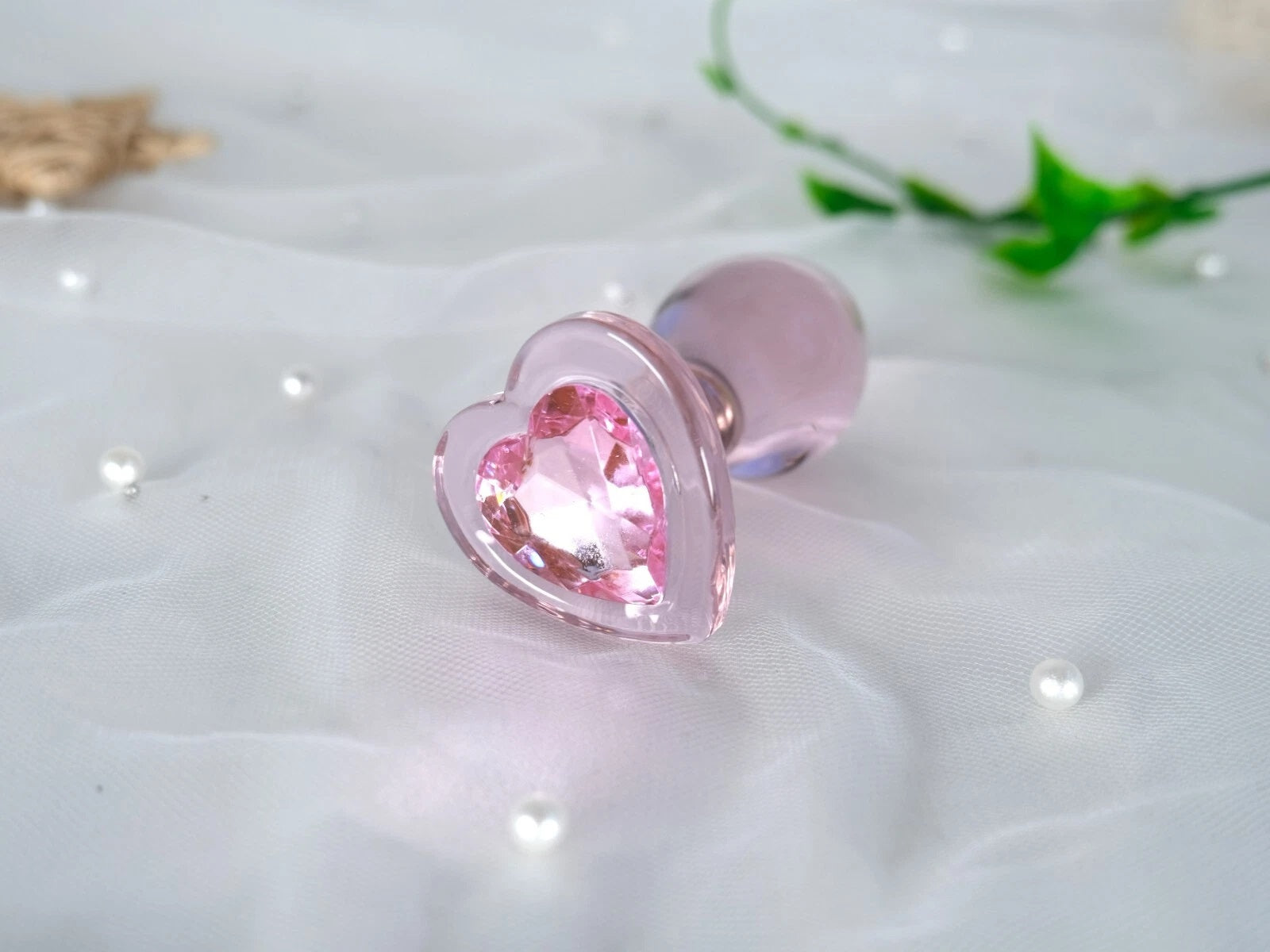 Smooth pastel pink glass plug with a wide decorative heart-shaped base
Romantic aesthetic shot of the pink crystal heart glass plug resting on white satin fabric next to a delicate rose.