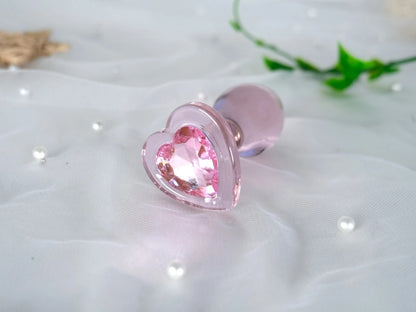 Smooth pastel pink glass plug with a wide decorative heart-shaped base
Romantic aesthetic shot of the pink crystal heart glass plug resting on white satin fabric next to a delicate rose.