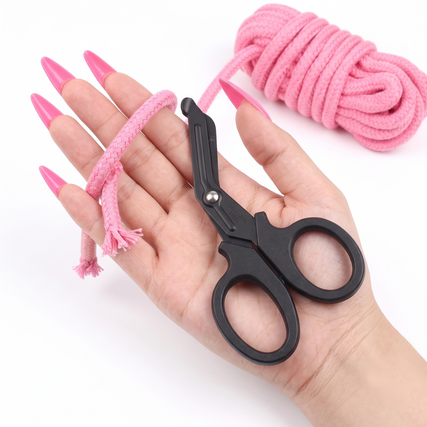 A hand displaying the black safety shears alongside a cleanly cut piece of pink bondage rope, demonstrating the blade's sharp cutting power.