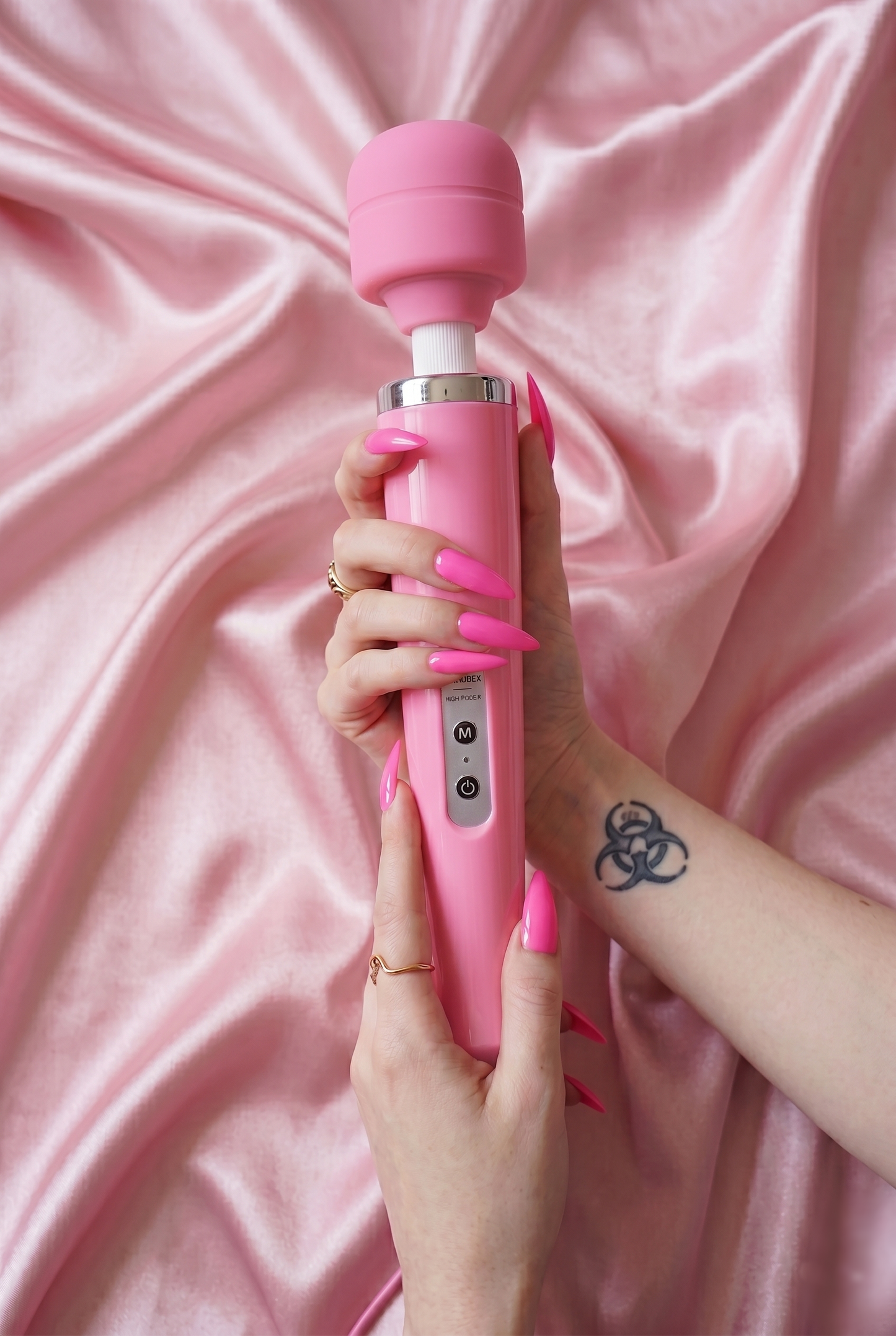 Close-up of a hand gripping the pink magic wand massager upright against soft pink satin sheets, ready for intense clitoral stimulation and full body massage.