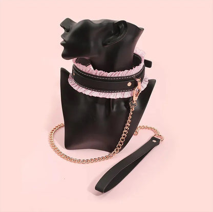 The premium black leather cuffs with pink ruffles tucked into a luxury black satin storage pouch with a gold chain leash draped over it.