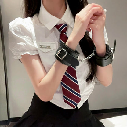 A model in a schoolgirl uniform aesthetic wearing secure black fluffy lined faux leather wrist cuffs connected by a silver chain.
