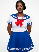Model wearing a short-sleeved white onesie with blue sailor collar, red chest bow, and matching blue pleated schoolgirl skirt with white hem stripes, standing 