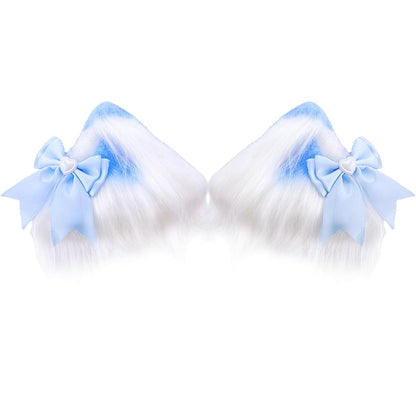 A close-up of two-tone fluffy kitten play ear clips with a white base and pastel blue tips, adorned with a light blue satin bow and a delicate silver heart-shaped centerpiece.