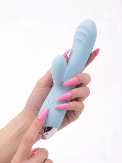 A hand with long pink nails holding the ice blue Pastel Dream Rabbit Vibrator, pointing at the elegant control buttons on the metallic base