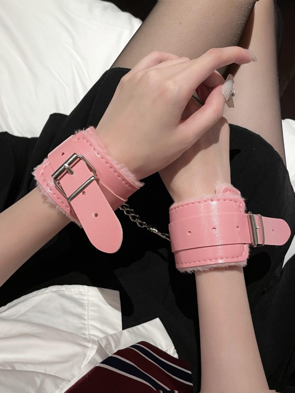 A close-up lifestyle shot of a person's wrists securely bound by adorable pastel pink fluffy faux leather cuffs.