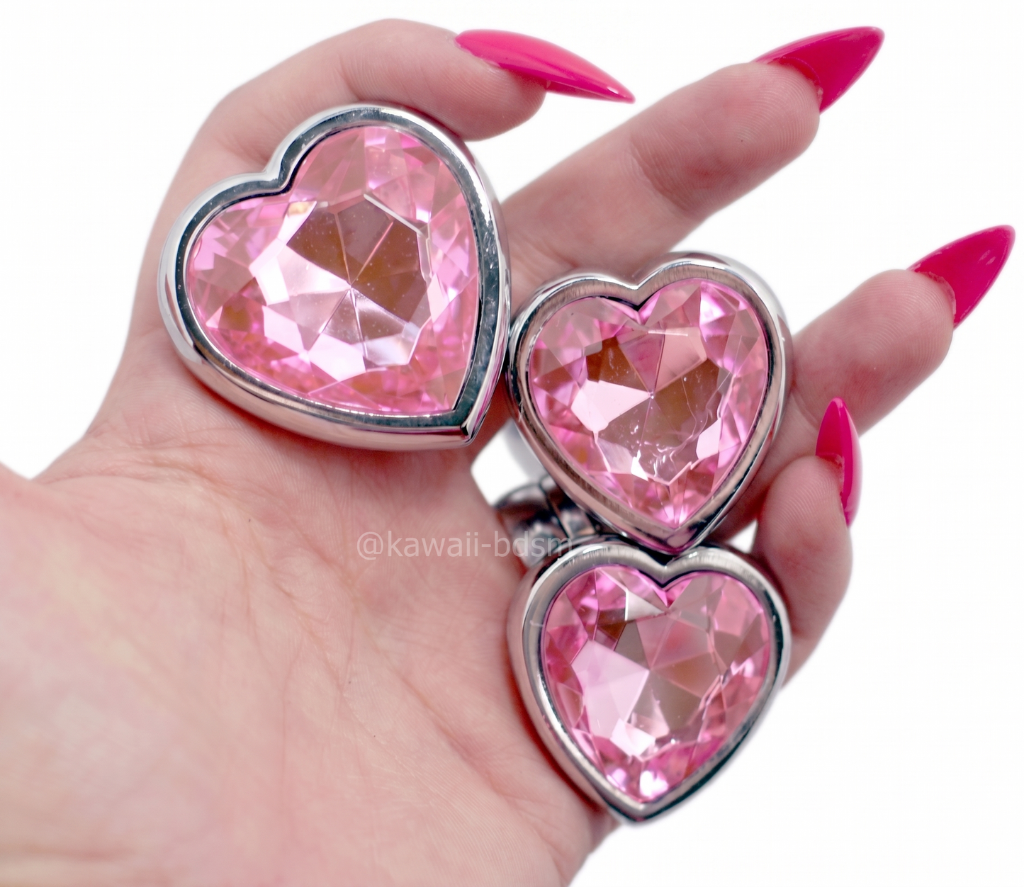 Close-up of a hand holding three pastel pink crystal heart metal plugs, showcasing the beautifully flared gem bases.