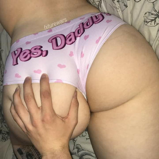 Close-up shot of a model wearing light pink heart-print panties, emphasizing the bold bubble font of the "Yes, Daddy?" text on the back.